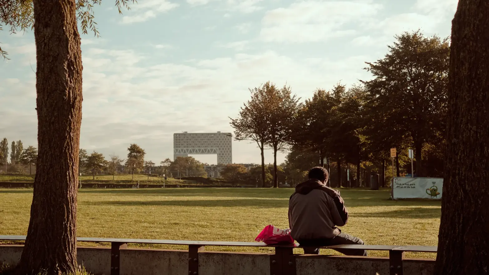 Man op bankje in het Westerpark, op de achtergrond de Pontsteiger